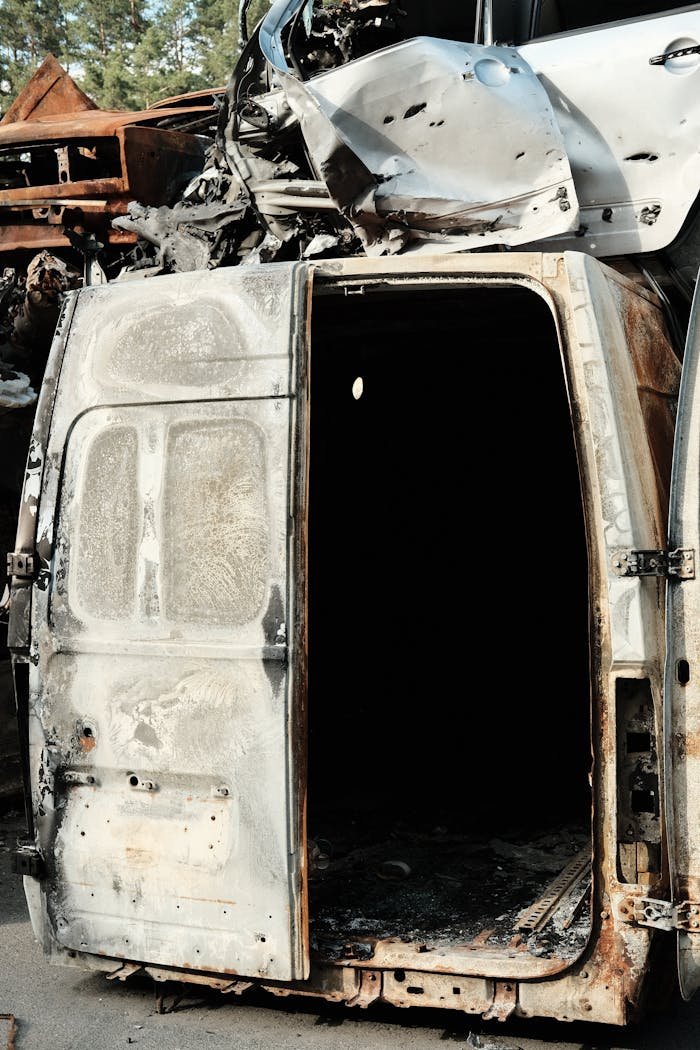 A destroyed van amidst a pile of wrecks in a junkyard, depicting stark neglect.